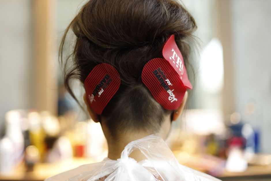 Imagem de uma pessoa com cabelo cortado na nuca, com adesivos de velcro de fita métrica na cabeça, sugerindo uma transformação ou mudança de visual em um ambiente de salão ou barbearia.
