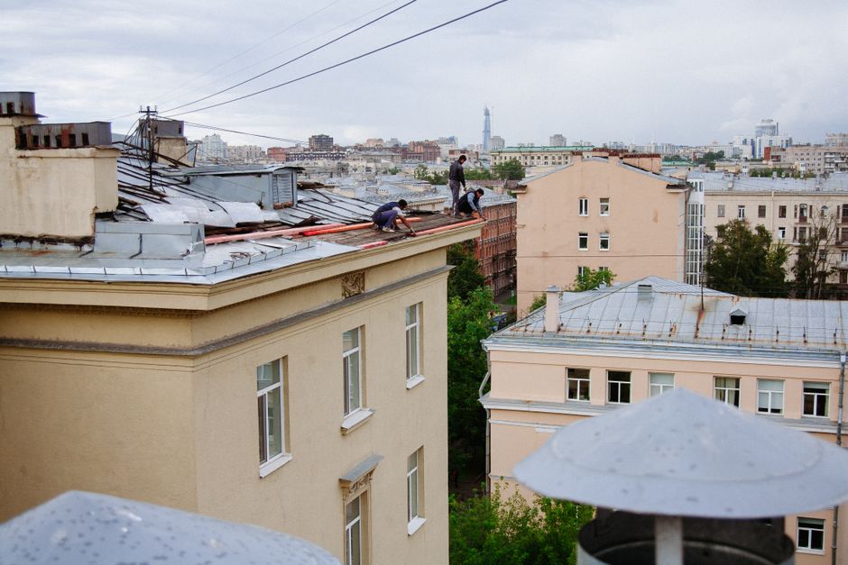 Homens trabalhando na manutenção e instalação de telhados em edifícios urbanos, demonstrando atividades de construção civil e reparos em altura.