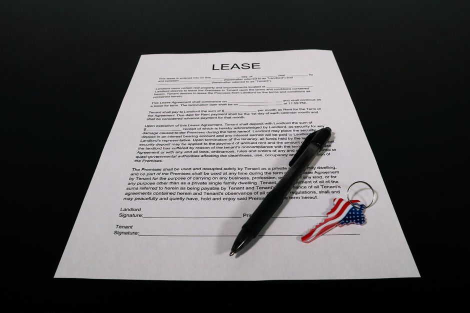 Imagem de um contrato de locação com uma caneta e uma chave decorada com a bandeira dos Estados Unidos, simbolizando negócios imobiliários ou acordos comerciais internacionais.