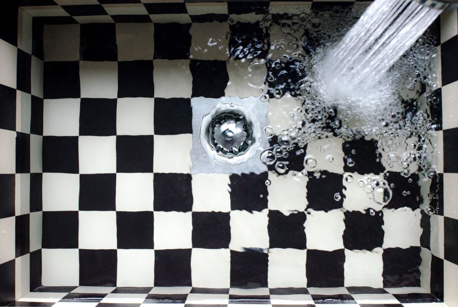 Imagem de uma pia de cozinha com um padrão de azulejos em preto e branco, com água escorrendo do dispensador.