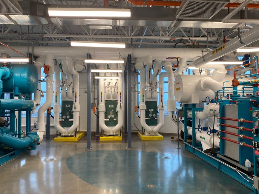 Imagem de uma sala técnica industrial com tubulações e equipamentos de vedação, destacando a infraestrutura de um sistema de circulação de fluidos ou energia.