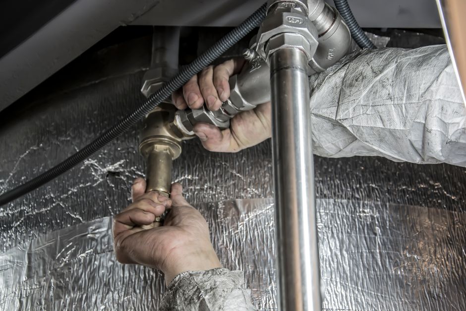 Técnico realizando manutenção em sistema de encanamento ou tubulação industrial, focando na instalação ou reparo de conexões de tubos metálicos.