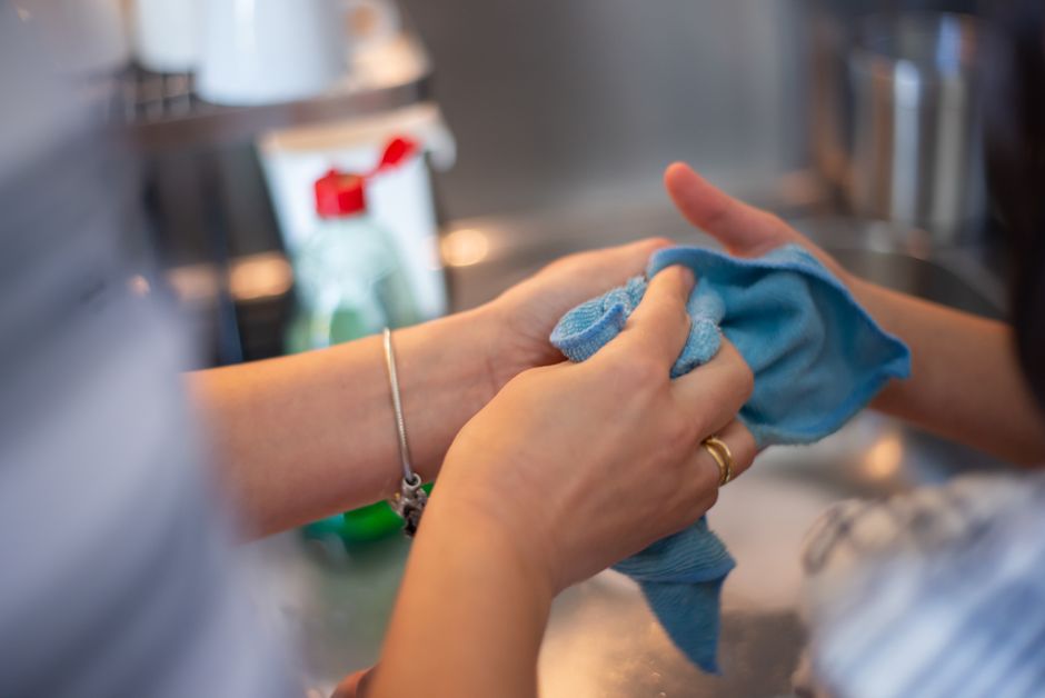 Mãos lavando utensílios na cozinha, representando cuidado e higiene na rotina doméstica.