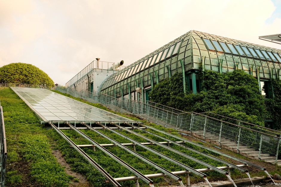 Imagem de uma estrutura de vidro com elementos sustentáveis, incluindo painéis solares e vegetação, representando inovação e sustentabilidade.