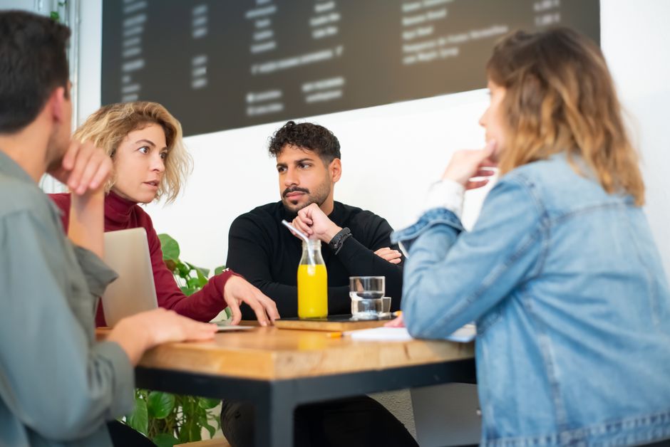 Grupo de pessoas em uma reunião de discussão sobre estratégia ou projeto, com uma tela grande ao fundo exibindo informações digitais.