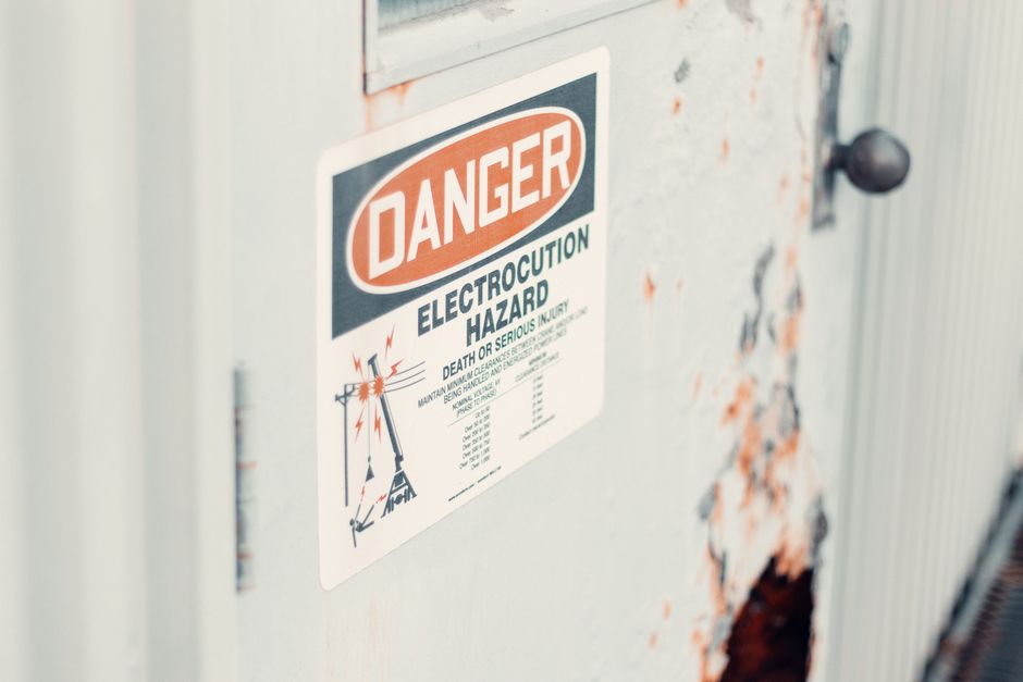Imagem de um aviso de perigo elétrico em uma cabine de distribuição de energia, alertando sobre riscos graves de choque.