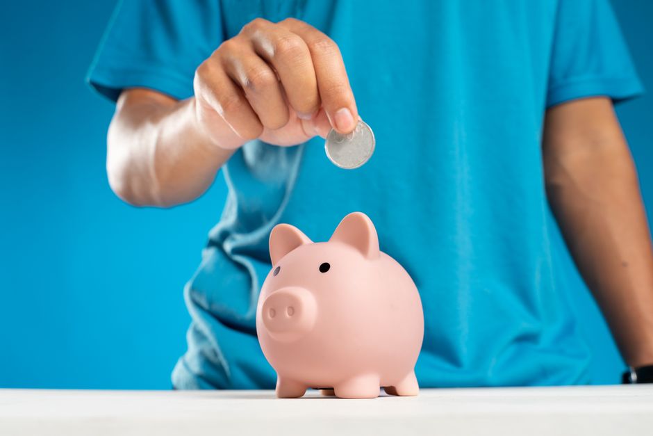 Pessoa colocando uma moeda em um cofrinho para ilustrar economia e planejamento financeiro.