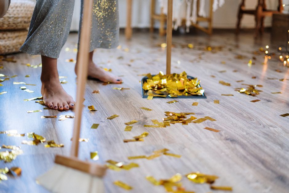 Pessoa comemorando uma conquista ou celebração em um ambiente festivo com confete dourado espalhado pelo chão.