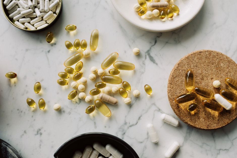 Imagem de diversas cápsulas e comprimidos de medicamentos dispersos sobre uma bancada de mármore, simulando um tema relacionado a saúde e medicamentos.