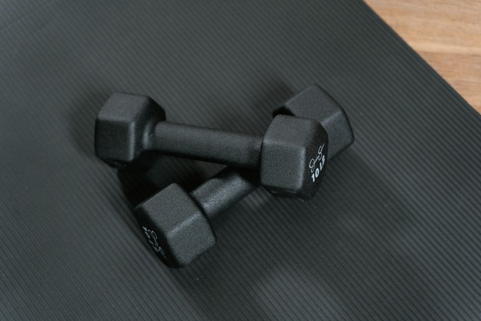 Par de halteres de academia sobre superfície escura, simbolizando exercícios físicos e saúde.