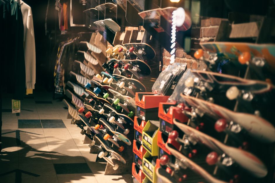 Imagem de uma loja de skate com prateleiras repletas de vários modelos de skate em um ambiente de shopping ou rua comercial.
