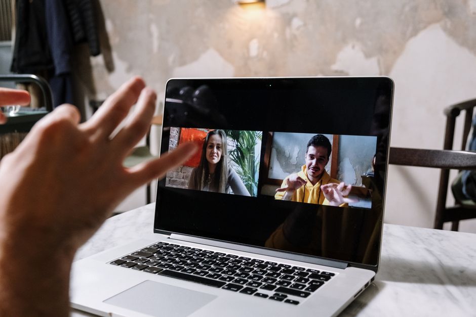 Pessoa participando de uma videochamada com duas pessoas, em ambiente que parece ser um espaço de trabalho ou café, destacando a comunicação virtual.