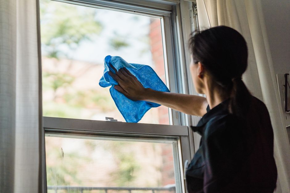 Mulher limpando a janela para manter o ambiente limpo e organizado, simbolizando cuidado com o espaço doméstico.