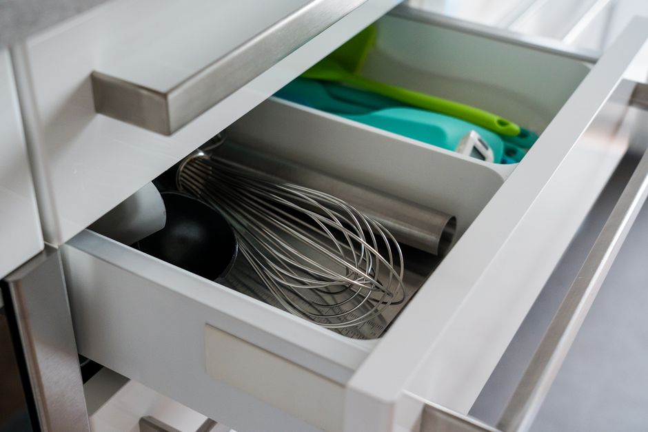 Imagem de uma gaveta de cozinha organizada com utensílios metálicos e itens de limpeza, ideal para ilustrar dicas de organização doméstica.