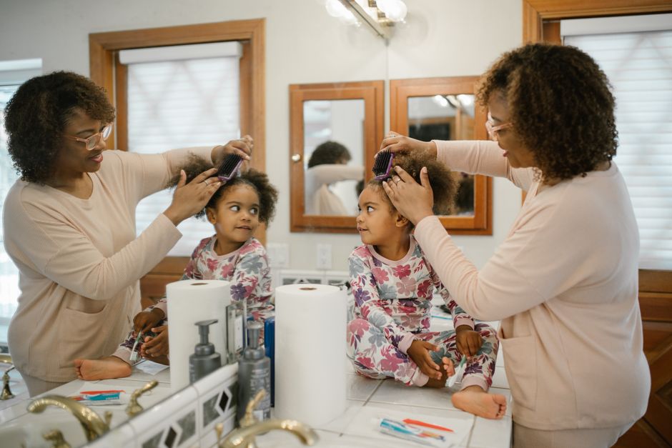 Mãe ajudando a filha a arrumar o cabelo no banheiro, momento de cuidado e relacionamento familiar.