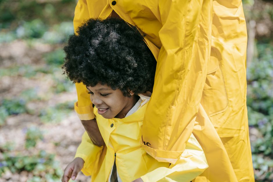 Criança sorridente participando de atividade ao ar livre em um ambiente natural, com um adulto ajudando na orientação.