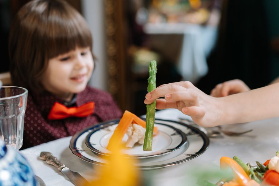 Criança brincando com comida em uma mesa de jantar, explorando alimentos de forma divertida.