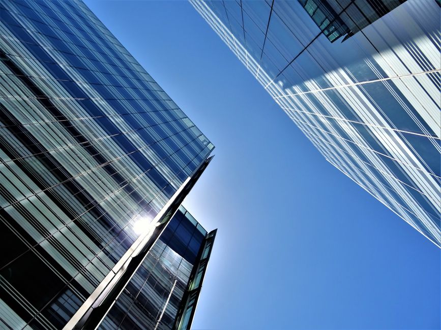 Imagem de arranha-céus de vidro refletindo o céu azul, simbolizando o mundo corporativo e inovação urbana.