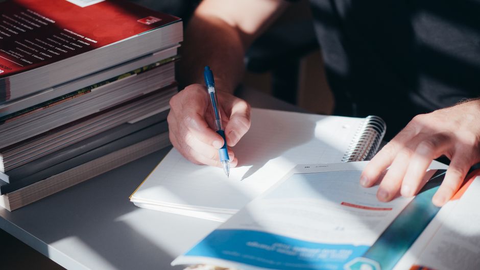 Pessoa organizando e revisando documentos em um ambiente de estudo ou trabalho, com foco em planejamento ou pesquisa.