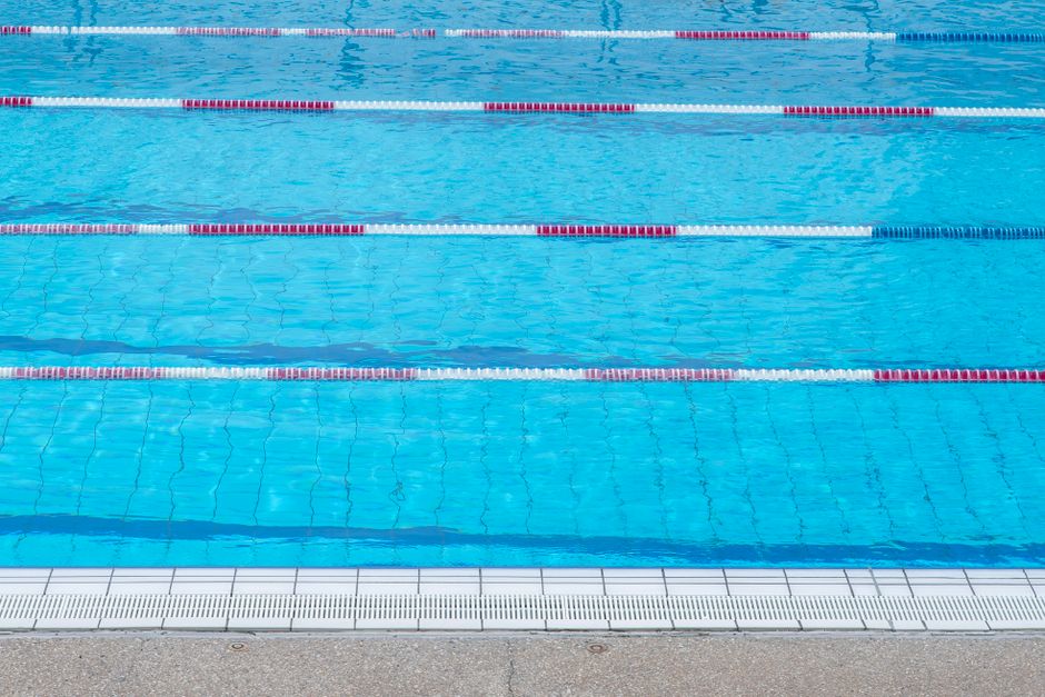 Imagem de uma piscina olímpica vazia, focada na água e nas raias de natação, ideal para ilustrar temas de esportes aquáticos ou lazer.