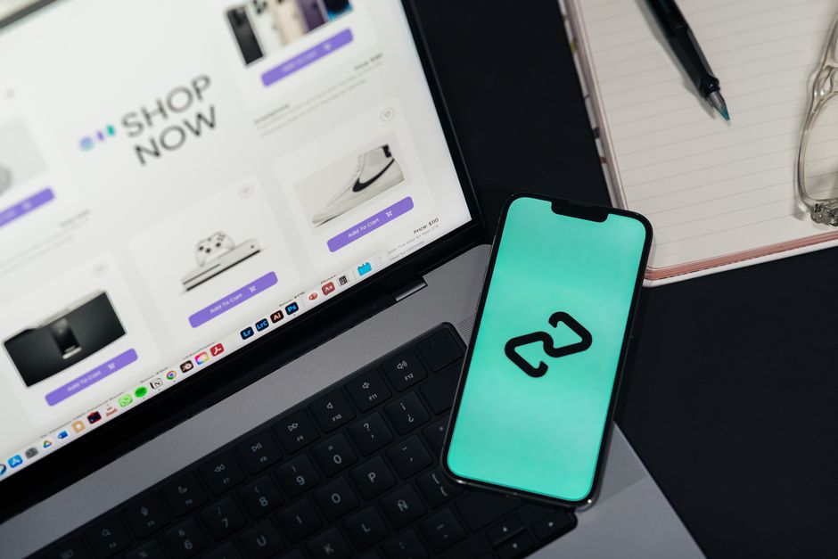 Imagem que mostra um ambiente de trabalho digital, com um laptop exibindo uma loja online, um smartphone com ícone de nuvem, ideal para artigos sobre comércio eletrônico e inovação tecnológica.