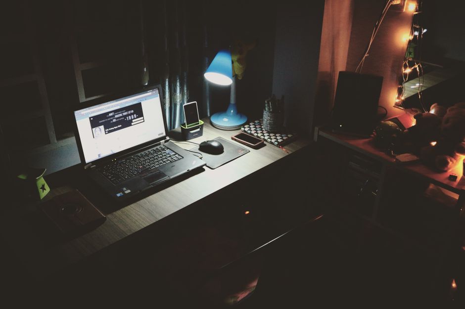 Estação de trabalho noturna com laptop, luminária azul e elementos de decoração que criam um ambiente acolhedor para estudos ou trabalho remoto.