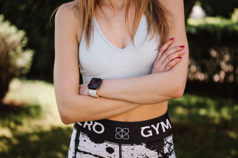 Mulher em roupas esportivas com braços cruzados em ambiente ao ar livre, representando saúde e bem-estar.