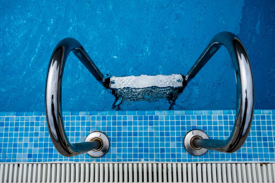 Escada de piscina de metal vista de cima, indicando o acesso à água e lazer.