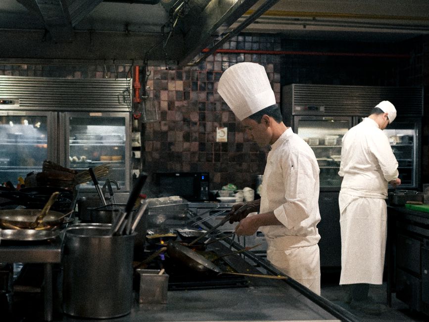 Cozinheiros profissionais preparando pratos em uma cozinha industrial de restaurante.