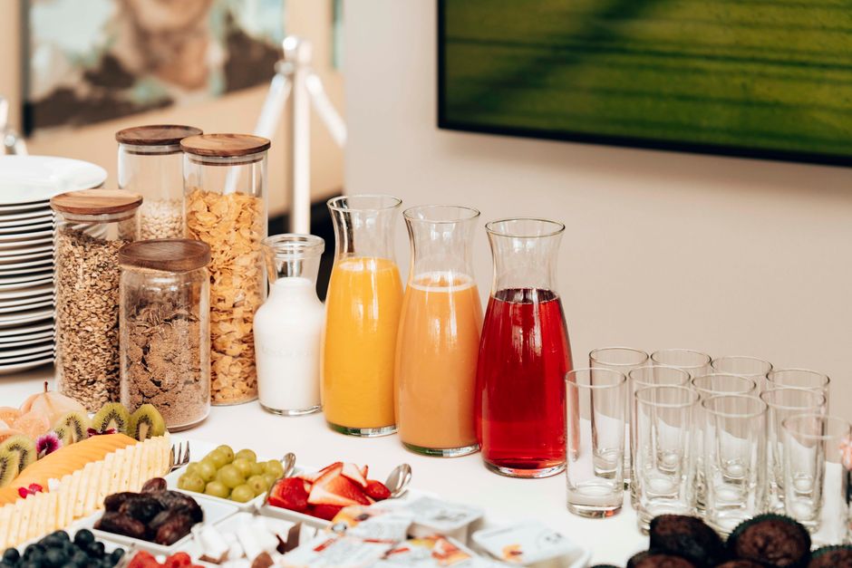 Imagem de um buffet de café da manhã com variedade de sucos, frutas e alimentos, ideal para ilustrar um artigo sobre alimentação saudável ou recepção de eventos.