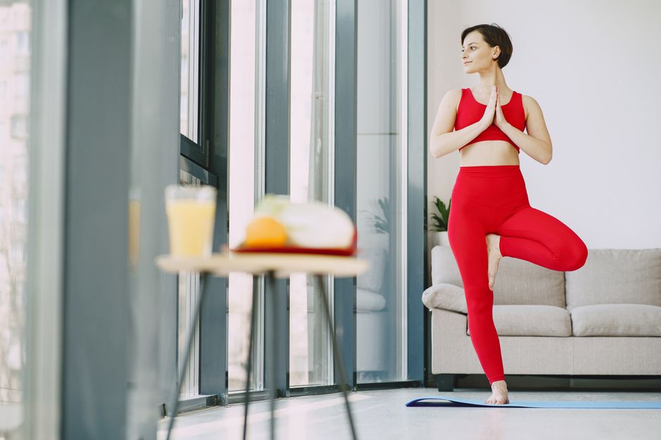 Mulher praticando yoga ao lado de uma janela com foco no bem-estar e equilíbrio pessoal.