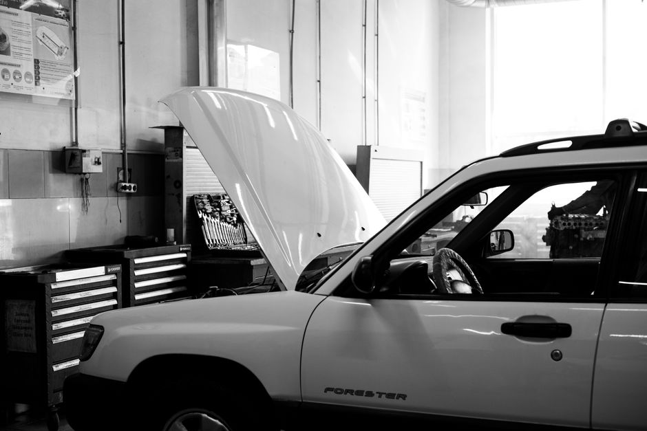Imagem de um carro em uma oficina mecânica, com o capô aberto, representando manutenção automotiva e reparo de veículos.