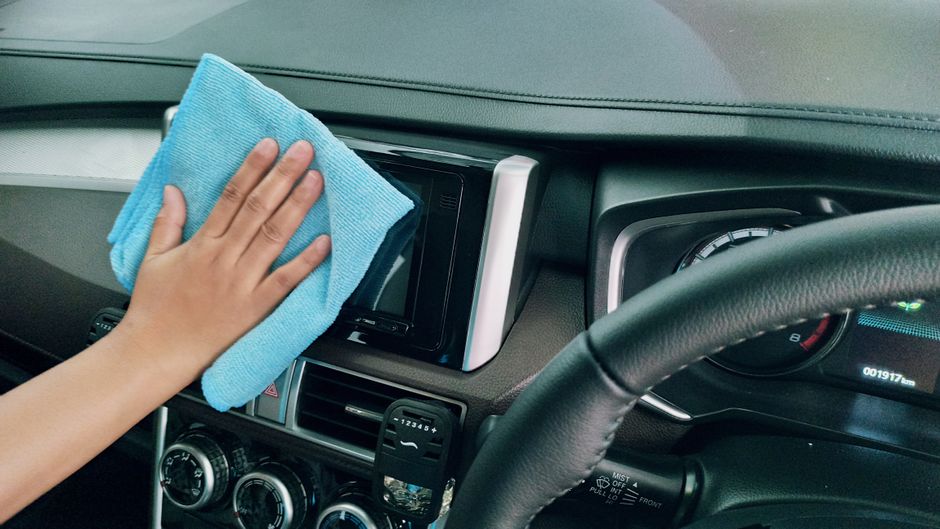 Pessoa limpando o painel do carro com um pano de microfibra, destacando a manutenção e cuidado com o veículo.