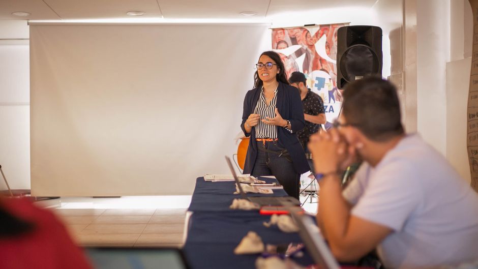 Mulher apresentando em um evento de treinamento ou palestra, envolvida com público em ambiente de negócios ou educação.
