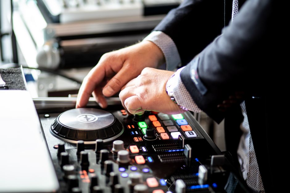 Profissional ajustando equipamento de DJ em ambiente de evento ou apresentação ao vivo, evidenciando foco em música e entretenimento.