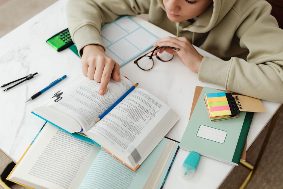 Estudante estudando para concurso ou vestibular, concentrado em materiais de leitura e organização do estudo.