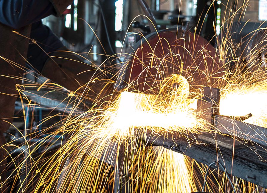 Imagem de soldador trabalhando com faíscas brilhantes em um ambiente industrial, destacando o ofício da soldagem e a manufatura.