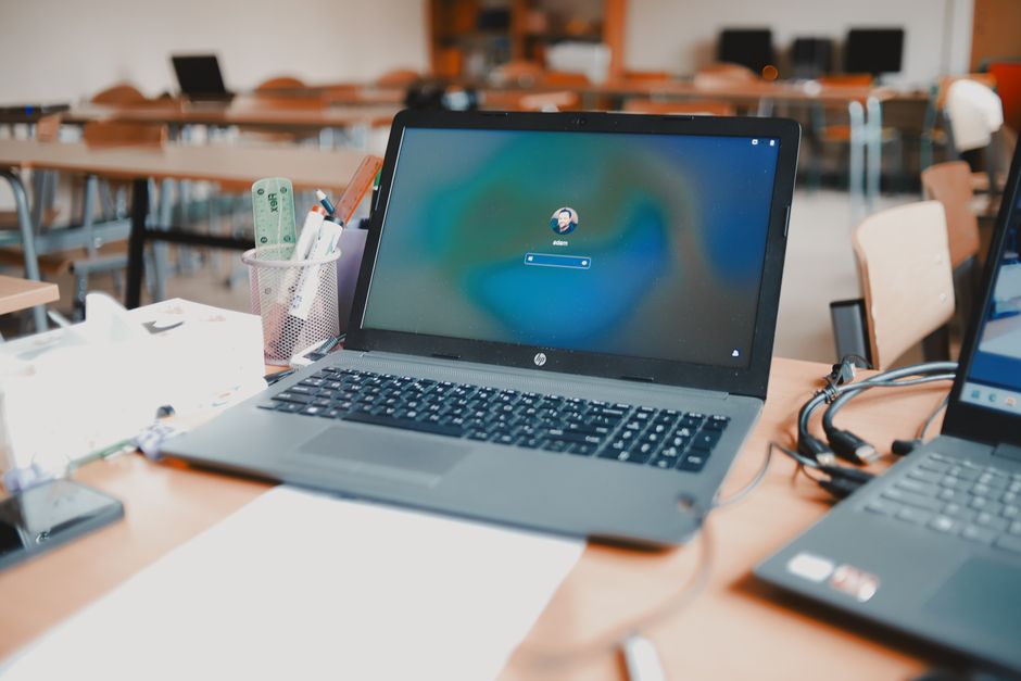 Imagem de um computador portátil em uma sala de aula ou reunião, sugerindo um ambiente de trabalho ou estudo remoto.