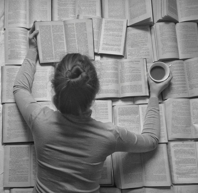 Pessoa estudando ou pesquisando com diversos livros e uma xícara de café sobre uma mesa.
