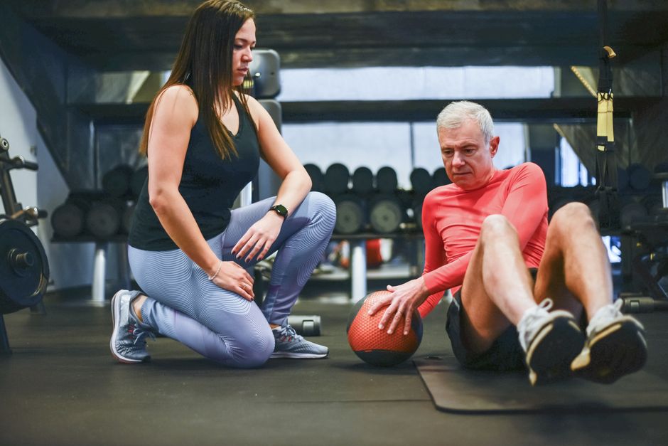 Instrutora ajudando um idoso a realizar exercícios de fisioterapia ou treinamento físico em uma academia.