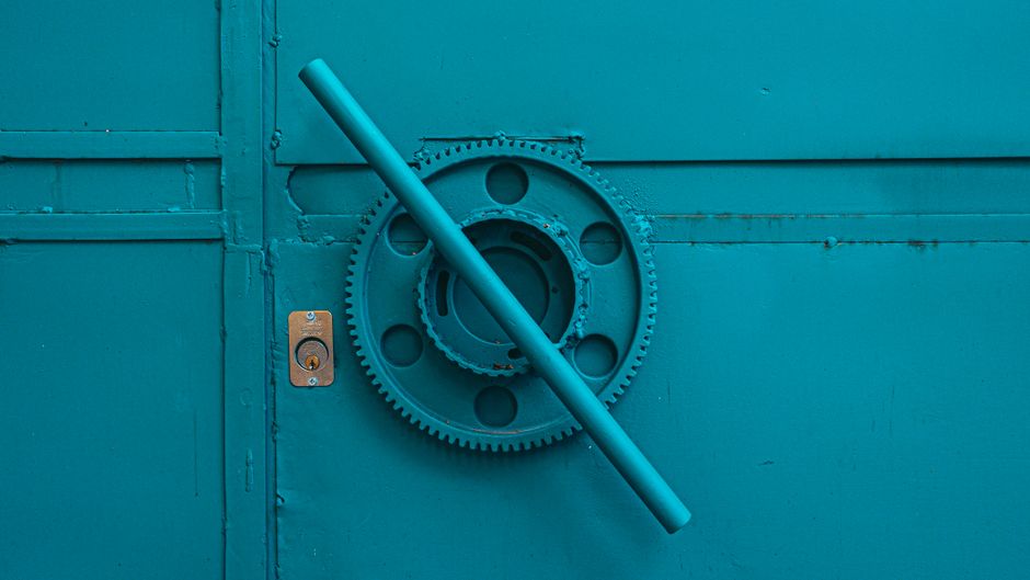 Imagem de uma porta de ferro azul fechada com um mecanismo de trava de segurança, simbolizando proteção e acesso controlado.