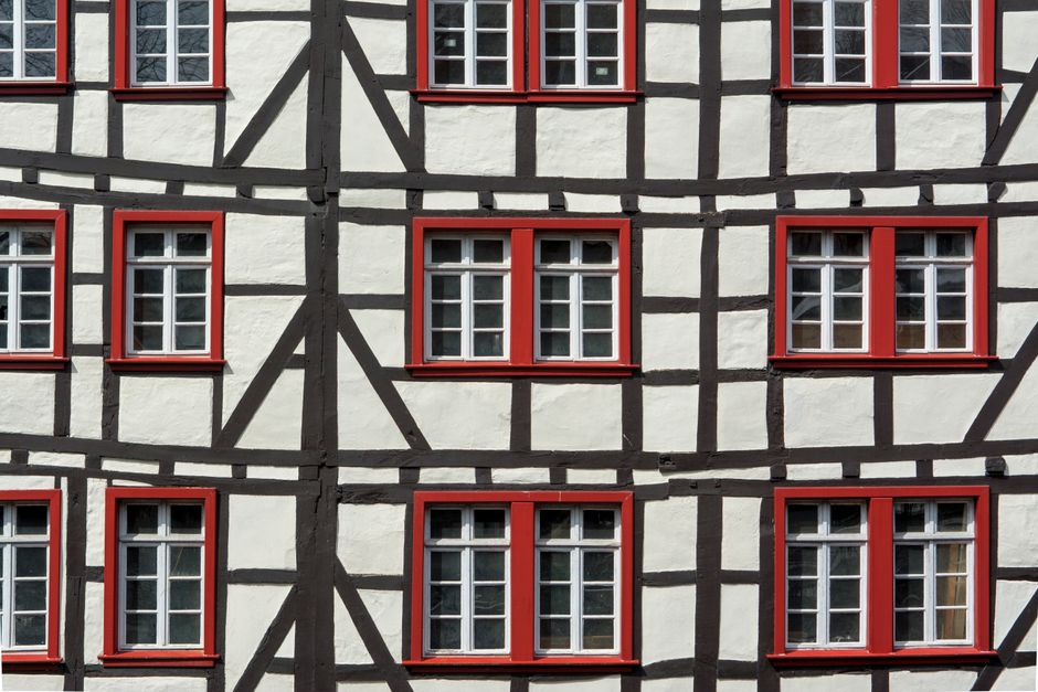 Fachada de uma casa de estilo tradicional com estrutura de madeira aparente e janelas com molduras vermelhas, ressaltando arquitetura característica e detalhes visuais marcantes.