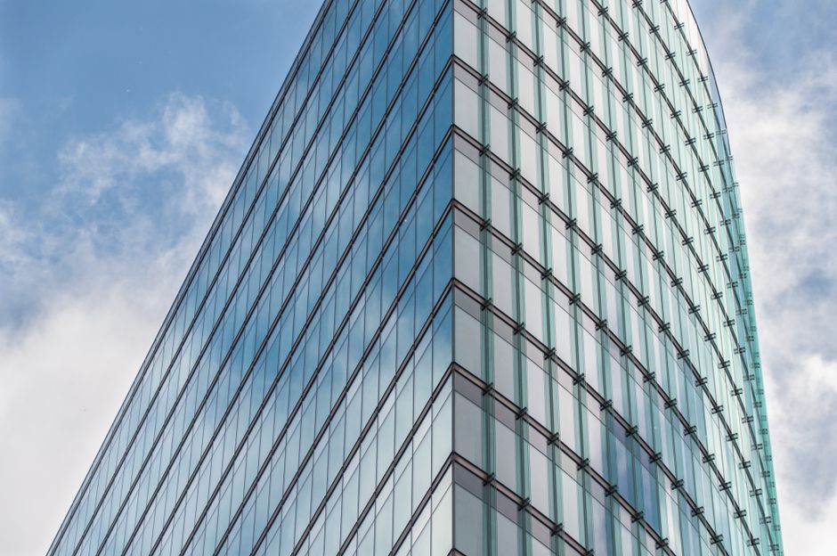 Foto de um arranha-céu de fachada moderna e de vidro refletindo o céu, simbolizando inovação e crescimento urbano.