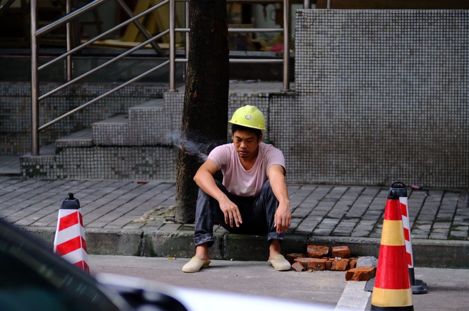 Homem cansado sentado na calçada após trabalho de reparo na rua, em um ambiente urbano.