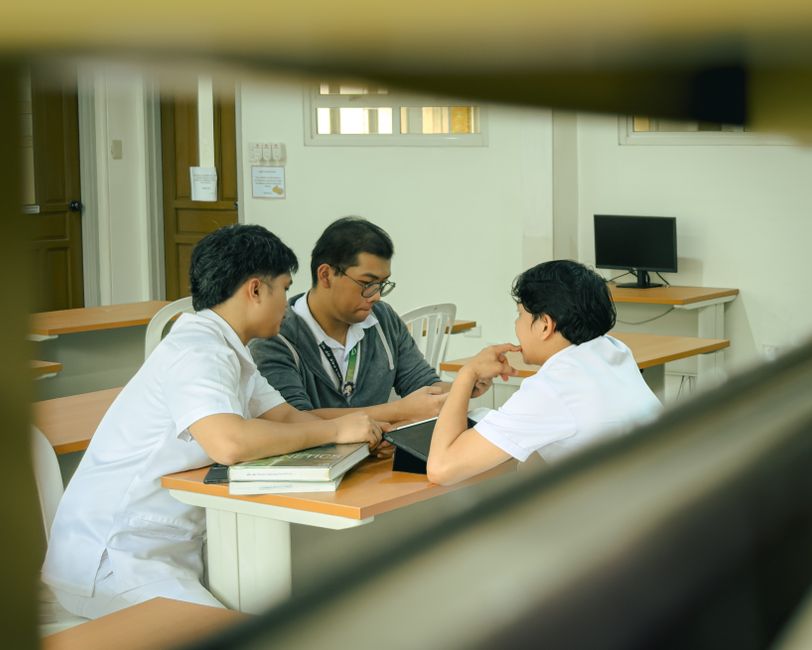 Três estudantes discutindo em uma sala de aula, focados no aprendizado e na troca de conhecimentos.