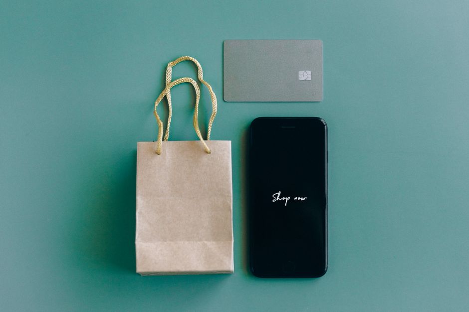 Imagem representando compras online e pagamentos digitais com cartão de crédito, smartphone e sacola de papel sobre fundo verde