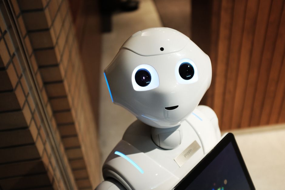 Robô com aparência amigável interagindo com tecnologia em ambiente moderno, simbolizando inovação e inteligência artificial.