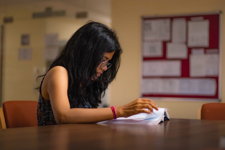 Jovem estudando ou revisando documentos em ambiente acadêmico ou de trabalho, destacando foco e concentração.