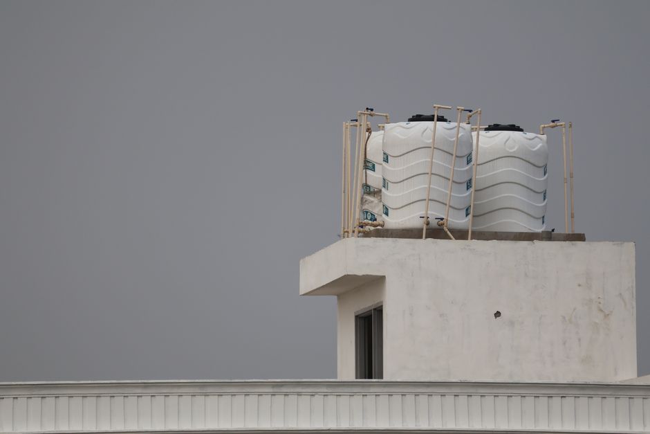 Imagem de um reservatório de água instalado no topo de um edifício residencial sob um céu nublado, simbolizando questões de infraestrutura urbana e abastecimento hídrico.