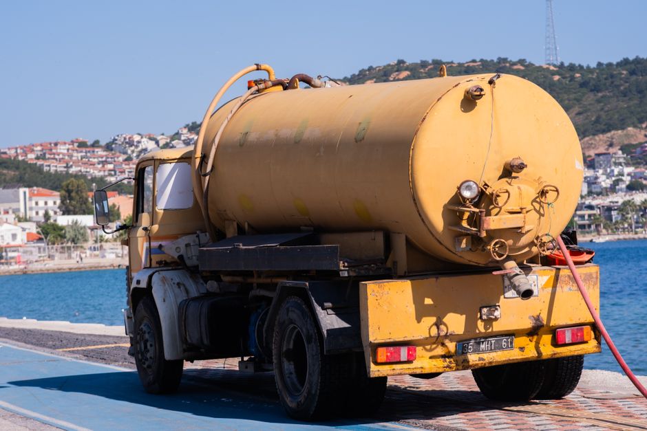 Caminhão de obras na orla marítima, utilizado para manutenção ou limpeza na área costeira.